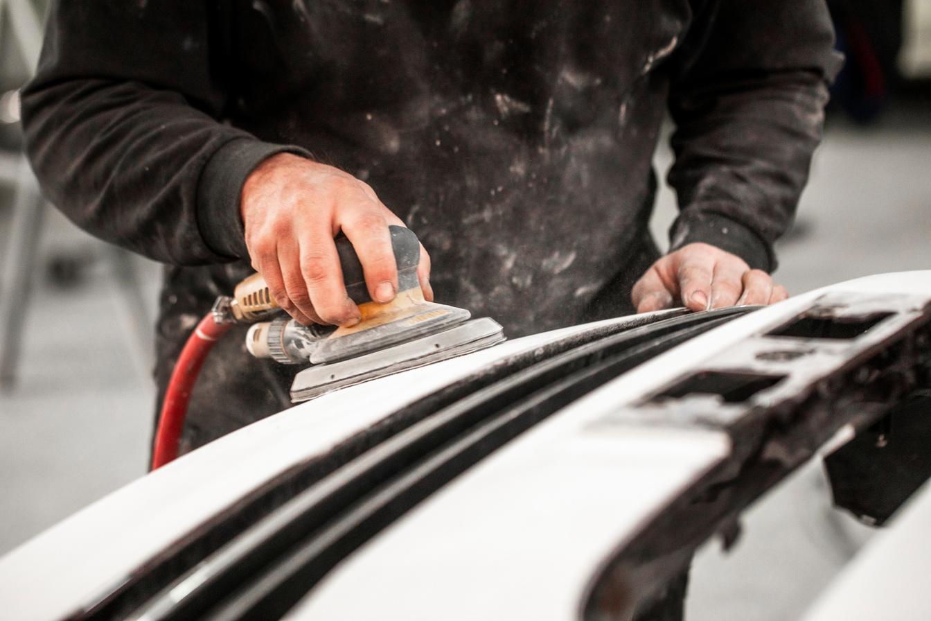 Body shop technician using a car buffer to buff out a surface on a car part in a painting booth of a body shop