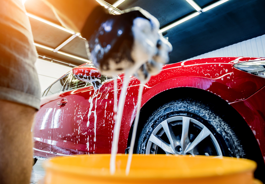 Worker washing red car with sponge on a car wash