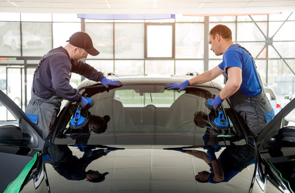 Automobile special workers replacing windscreen or windshield of a car in auto service station garage.